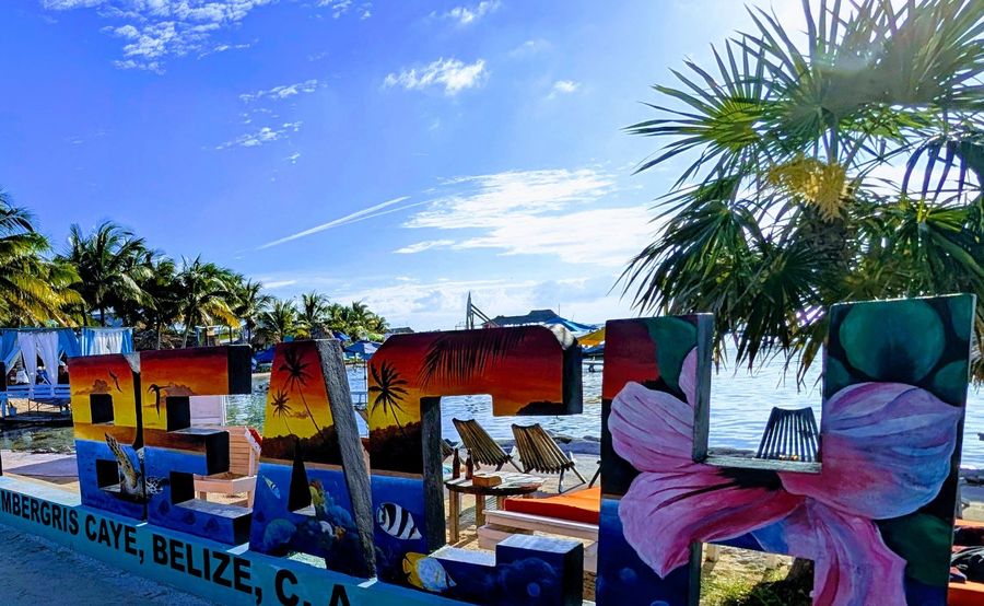 A painted Secret Beach sign under palm trees on Ambergris Caye