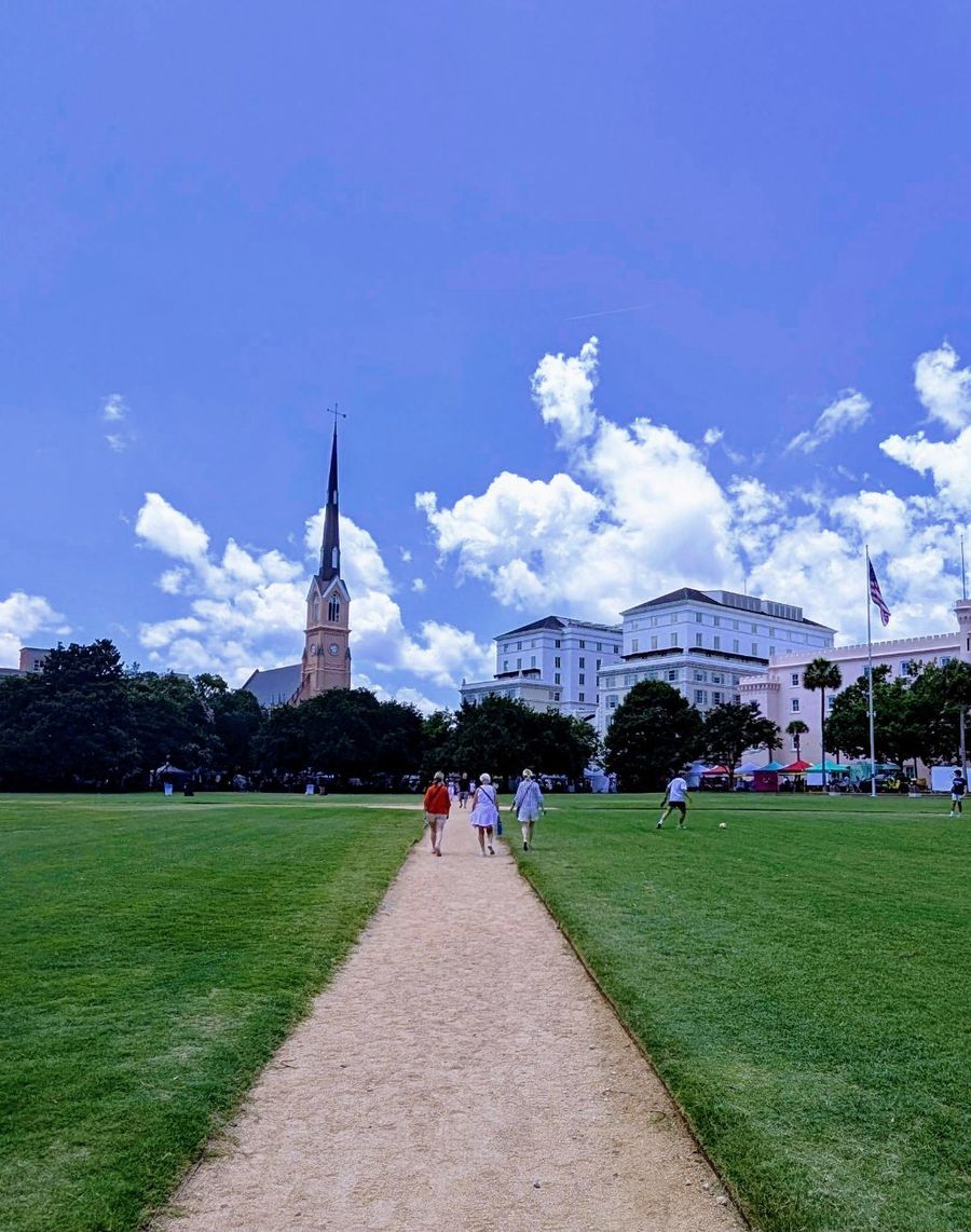 A path across a green square toward a church steeple and historic hotels